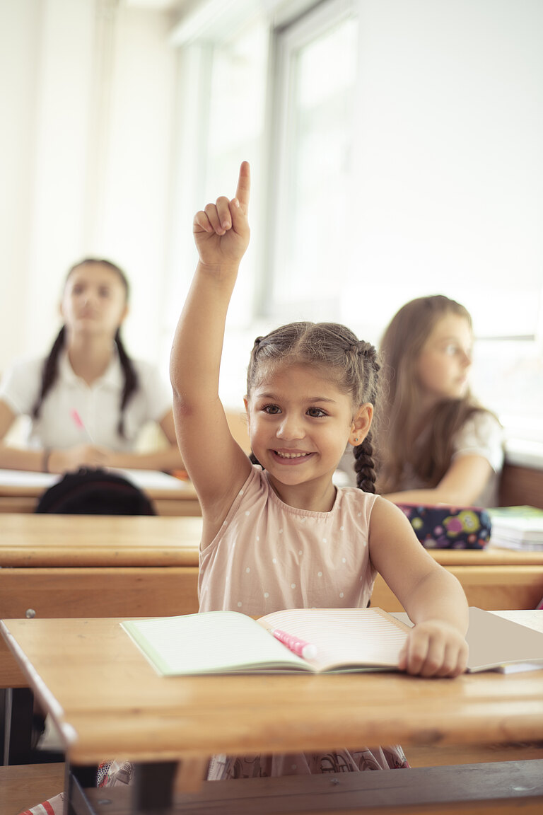 Unterricht im Klassenraum. Ein Grundschulmädchen meldet sich.